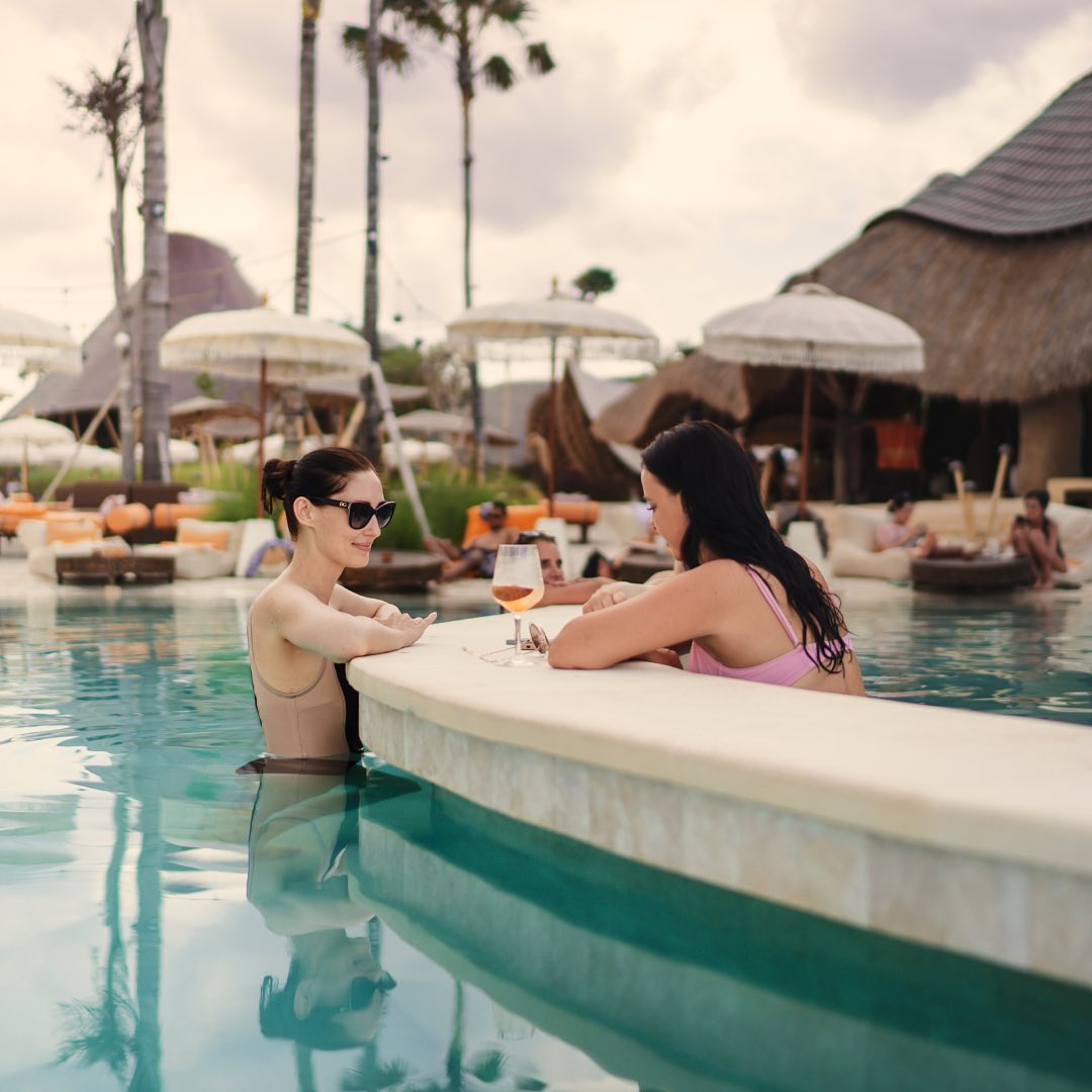 Two women are chatting in the swimming pool with a drink