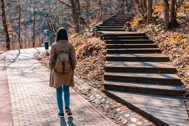 A woman in a brown coat and blue denim jeans walking on a wooden bridge